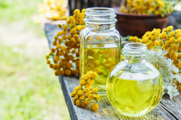 Tansy essential oil in a glass bottle on a wooden background near yellow tansy flowers. Tincture...