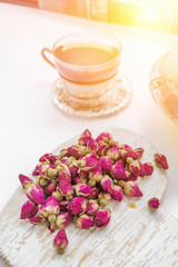 Tea made from rosebuds . Tea rose buds made from real rose buds, plucked young and then dried. A Cup of tea and a transparent teapot with a beautiful dish of pink buds