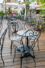 Openwork metal chairs and tables cafe wooden pavement street after the rain. Street cafe Porec, Croatia