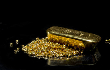 Gold bar on a pile of gold granules. Isolated on a black background.