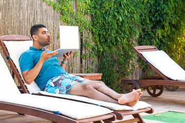 Portrait of disbelief bearded young adult freelancer man in blue t-shirt and shorts lying on cozy...