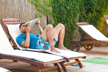 Portrait of suprised bearded young adult freelancer man in blue t-shirt and shorts lying on...