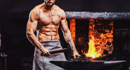Powerful bearded blacksmith with naked torso and protective apron is standing near working stove...