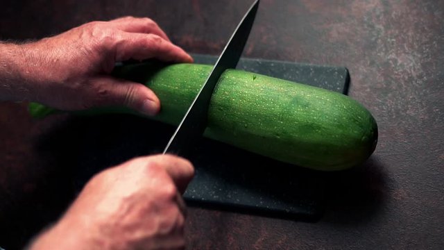 Closeup of male hands cutting courgette on the board, slow motion