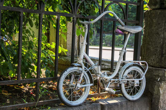 an old white painted children’s bicycle as a decoration chained to a garden fence