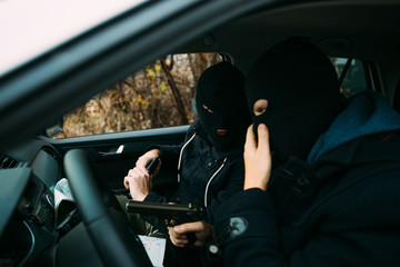 Bank robbers with their masks on pointing at the map prepared for robbing the bank,sitting in the car and waiting for the right time to rob.