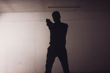 Silhouette of an armed man holding his gun and pointing with his laser beam at a target.