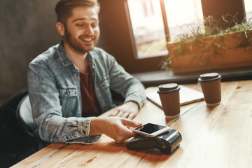 Secure way. Cheerful man in cafe is making a contactless smartphone payment