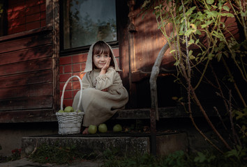 Dreaming girl with apples on a summer evening near the old house.