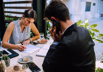 Two business partners discussing working plans in cafe bar while man talking on phone