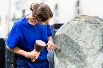 Stonemason working on boulder with sledgehammer and iron - obrazy, fototapety, plakaty
