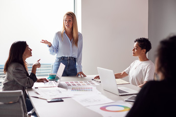 Female Boss Gives Presentation To Team Of Young Businesswomen Meeting Around Table In Modern Office
