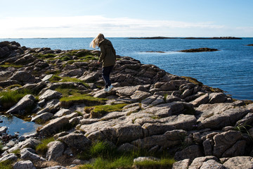 Fototapeta na wymiar A girl walks on the stones of coastline near the ocean. Beautiful nature landscape in North. Scenic outdoor view. Enjoy the moment, relaxation. Wanderlust. Travel, adventure, lifestyle. Explore Norway
