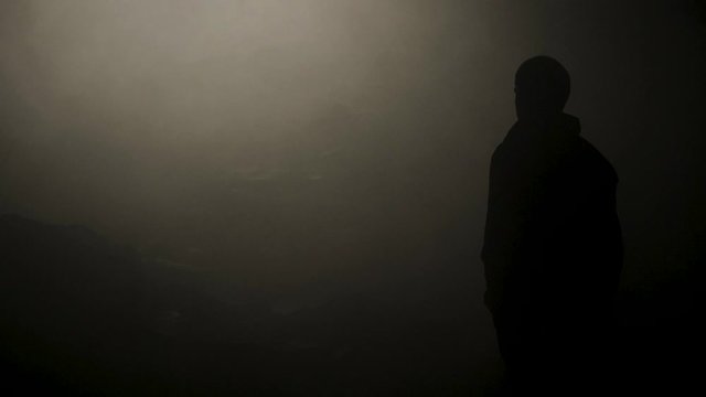Black silhouette of man in smoke cave. Stock footage. Faint light makes its way through thick fog illuminating details of cave and black silhouette of traveler
