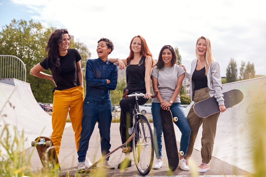 Portrait Of Female Friends With Skateboards And Bike In Urban Skate Park