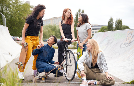 Portrait Of Female Friends With Skateboards And Bike In Urban Skate Park