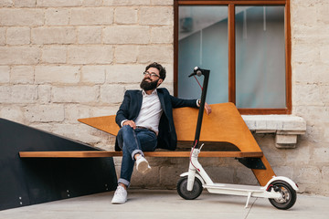 Stylish citizen relaxing on bench near eco electric scooter