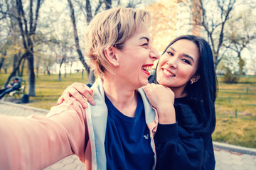 two young beautiful women close friends of different nationalities laugh and take a selfie in the park, a European and Asian, friendship day