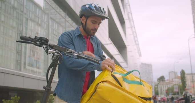 Closeup portrait of bearded caucasian delivery man delivering customer his order in city outdoors with cityscrapers