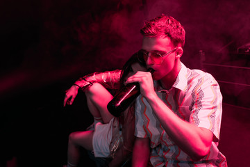 man with beer sitting near girl in nightclub during rave