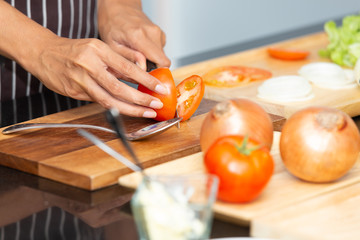Chef preparing salad and cuts vegetables with a knife. Vegetable slicing, preparation of vegetable salad. Cutting fresh tomato on cutting board.