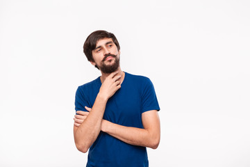 Obraz premium Thoughtful handsome brunet man in a blue shirt reflects on a good idea keeping one hand close to face standing isolated over white background.