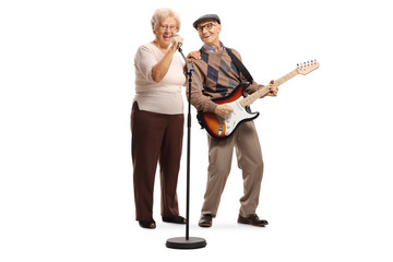 Elderly woman singing on a microphone and an elderly gentleman playing a guitar