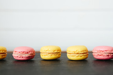 Sweet colorful French macaroon cookies dessert on black stone surface over white wooden background