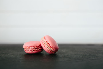 Sweet colorful French macaroon cookies dessert on black stone surface over white wooden background