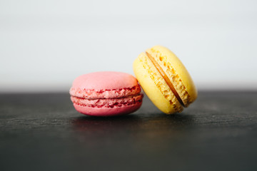 Sweet colorful French macaroon cookies dessert on black stone surface over white wooden background