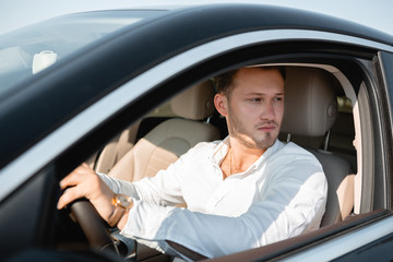 Successful businessman in a white shirt drives his luxary car.
