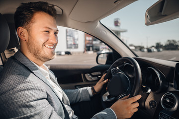 Happy driver in a suit in his luxary car listening to music and enjouying life. Concept of success.