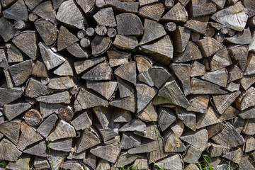 Background of dry chopped firewood laid in a woodpile. Grass at the pile of firewood.Grass at the pile of firewood. Close-up.