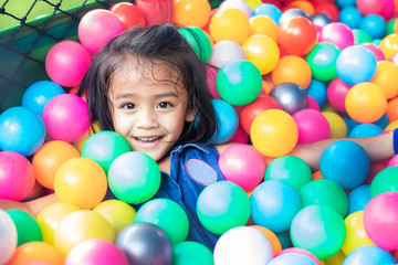 Fototapeta na wymiar Happy little girl sitting in colourful balls. little girl with colored plastic balls. Funny child having fun indoors.