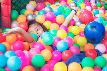 Fototapeta na wymiar Happy little girl sitting in colourful balls. little girl with colored plastic balls. Funny child having fun indoors.