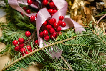 Spruce tree twig with green needles closeup and blurry pink satin ribbon and defocused artificial red berries. Red and green Christmas decorations. Winter holiday background with copy space