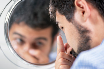 Man putting on contact lens in ophthalmology clinic . 
