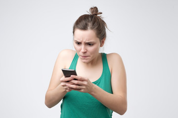 Naklejka premium Young caucasian woman in green shirt looking at phone with irritation. Virus on her phone concept.