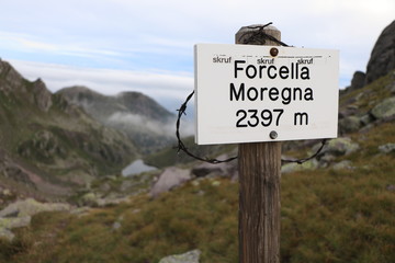 forcella moregna sign with narbed wire with mountain and lake on background