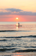 Fototapeta premium Woman's silhouette on a paddle board (SUP) at a beautiful pink pastel gradient sunset.