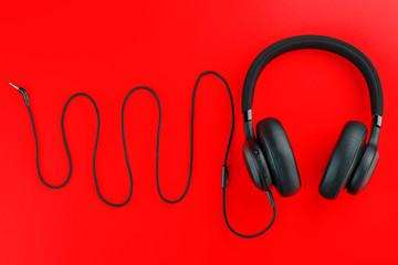 Hi-fi headphones on a red background with a wire in the form of a meandering sound wave. Sound frequency from the headphone wire