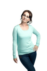 A girl in a mint-colored jumper, blue jeans and round glasses poses, llooking into the camera, a hand on her hip. Isolated on white background.