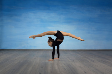 Girl gymnast in a black gymnastic swimsuit makes handstand on a blue sky background.