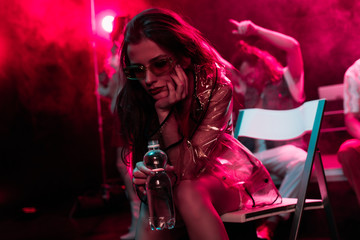 Fototapeta na wymiar sick young woman sitting with bottle of water in nightclub