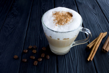 Coffee latte with cinnamon in the glass cup on the black wooden background. Closeup. Copy space.