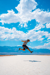Death Valley, California / United States »; August 2019: A young man jumping with a blue shirt on the white salt of Badwater Basin