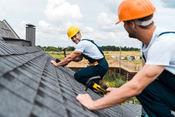 selective focus of happy repairman looking at coworker on roof © LIGHTFIELD STUDIOS