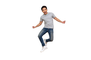 Excited Asian young man in gray t-shirt jumping while celebrating success isolated over white...