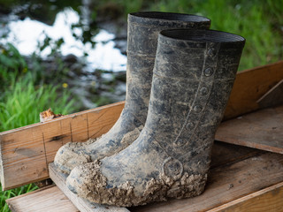 Black rubber wellington boots (wellingtons) outdoor on a wooden surface with mud and grass...