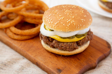 Homemade Mississippi Slug Burger with onion rings on a rustic wooden board on a white wooden table, side view. Close-up.